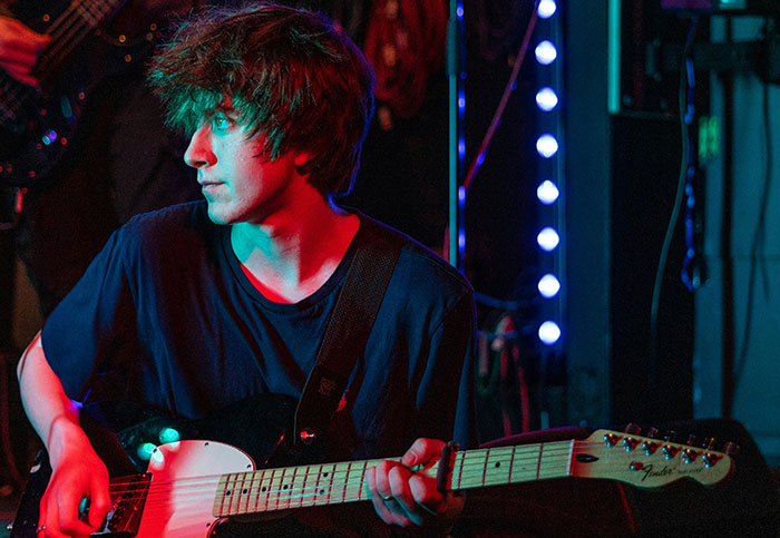 Young man playing electric guitar on stage with dramatic lighting, capturing an intense moment in live music performance.