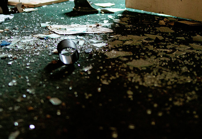 Broken glass scattered on a dark floor in a dimly lit room, illustrating accidental destruction and blown up life.
