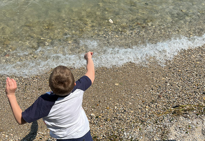 Young boy throwing stones into clear water at a pebble beach, illustrating moments that can affect someone's life unexpectedly.