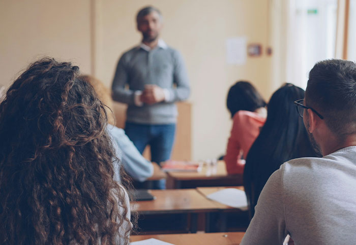 A man speaking to a group in a classroom setting, illustrating how people unintentionally blew up someone else's life.