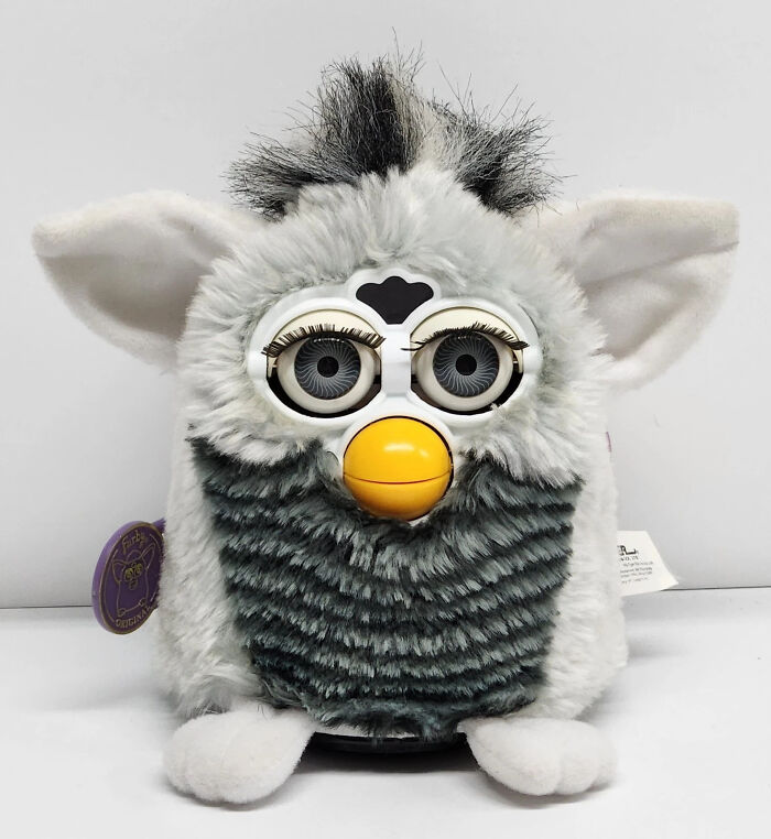 Vintage toys worth fortune Furby collectible with grey and white fur and large eyes sitting on a white surface.