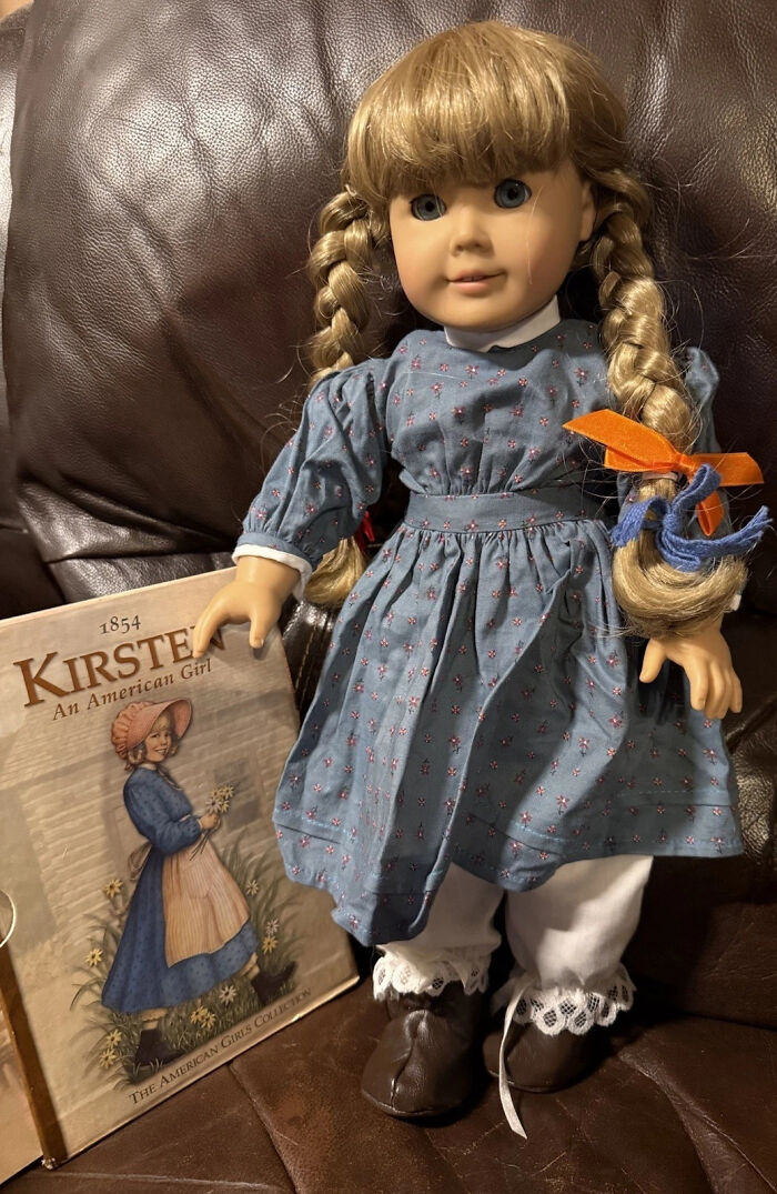 Vintage toys worth fortune American Girl doll Kirsten in blue dress with braided hair sitting on leather couch next to book