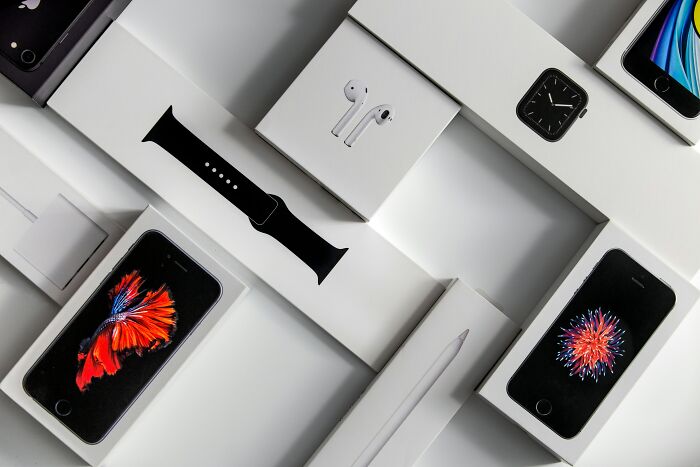 Various Apple product boxes including iPhones, Apple Watch, AirPods, and accessories representing companies sabotaging products.