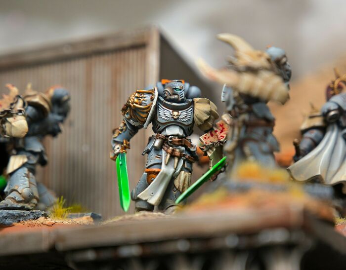 Detailed miniature figures of futuristic warriors with glowing green swords in a battle scene, illustrating secret stories theme.