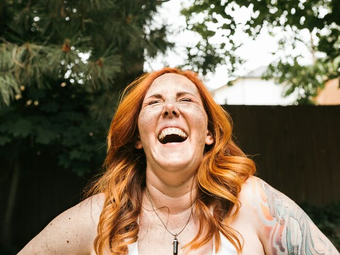 Red-haired woman laughing outdoors with tattooed arm, capturing a moment of people knowing they were dating an idiot.