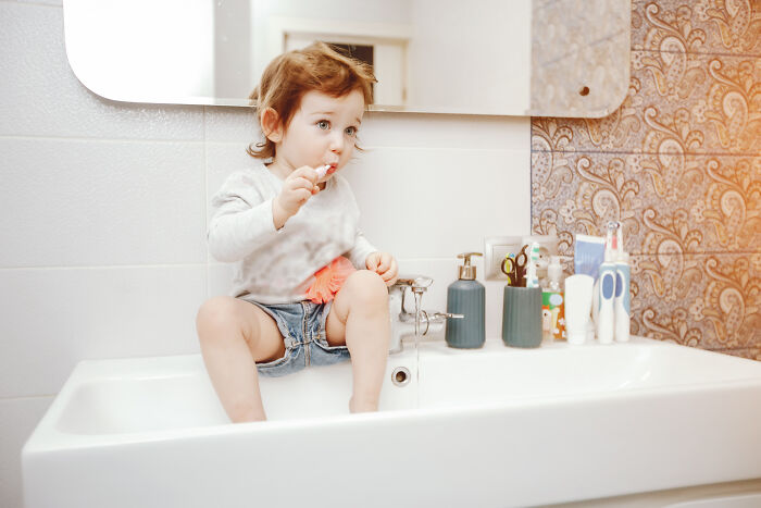 Toddler sitting in a bathroom sink brushing teeth, illustrating a babysitter’s unexpected bedtime story horror experience.
