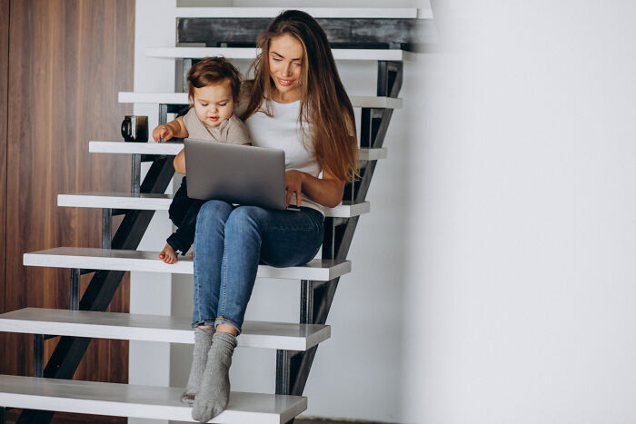 Babysitter and toddler sitting on stairs using laptop, illustrating babysitters’ bedtime stories and horror experiences.