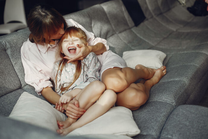 Babysitter and child laughing together on couch during bedtime, capturing a warm moment in babysitting experience.
