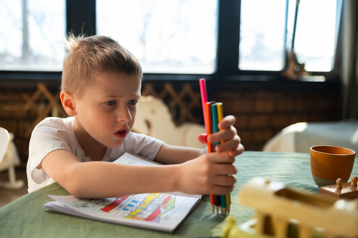 Young boy focused on stacking colored pencils at a table, illustrating babysitters sharing bedtime story horror experiences.
