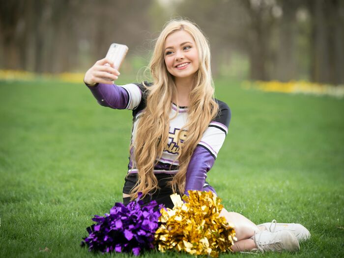Cheerleader sitting on grass taking a selfie, representing school bullies and their life after school stories.