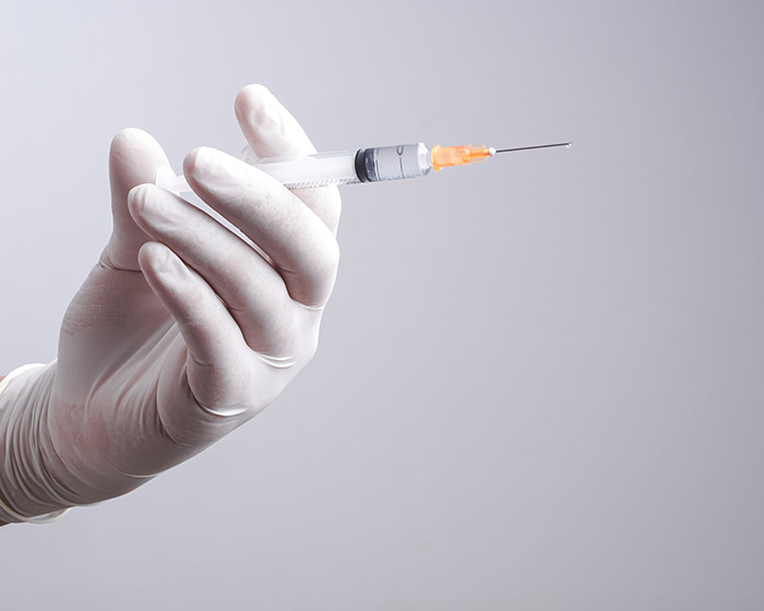 Hand in white glove holding a syringe with needle, representing Scrotox cosmetic trend and medical warnings for men.