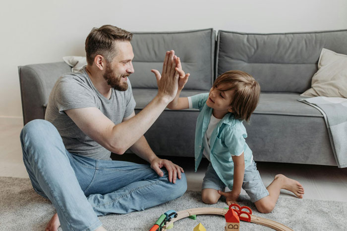 Man giving high five to young boy playing with toys on carpet, illustrating lazy entitled disabled bro situation.