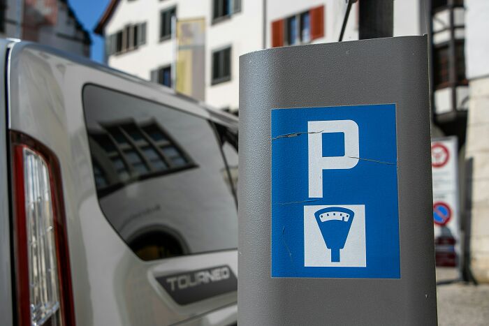 Parking meter with a blue sign in an urban area, illustrating busy streets where butcher and gravedigger professions intersect.