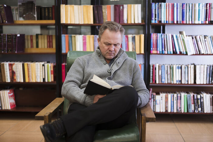 Man reading a book in a library surrounded by shelves, illustrating insider tricks employees use to make jobs easier.