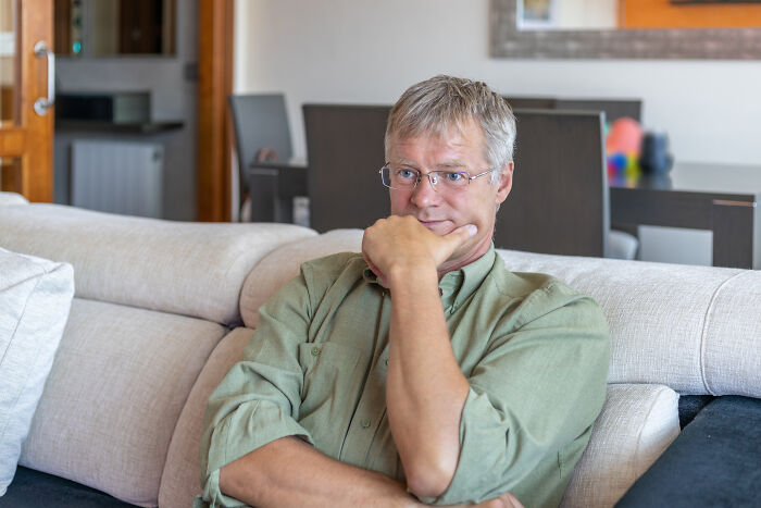 Middle-aged man sitting on a couch looking thoughtful and concerned, reflecting on dark family secrets discovered.