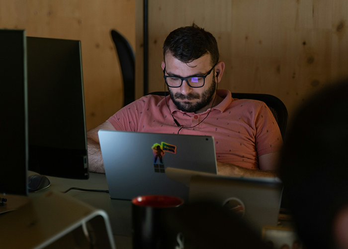 Man wearing glasses working late on laptop in dim office, illustrating server down business hours malicious compliance scenario. Man wearing glasses working late on laptop in dim office, illustrating server down business hours malicious compliance scenario.