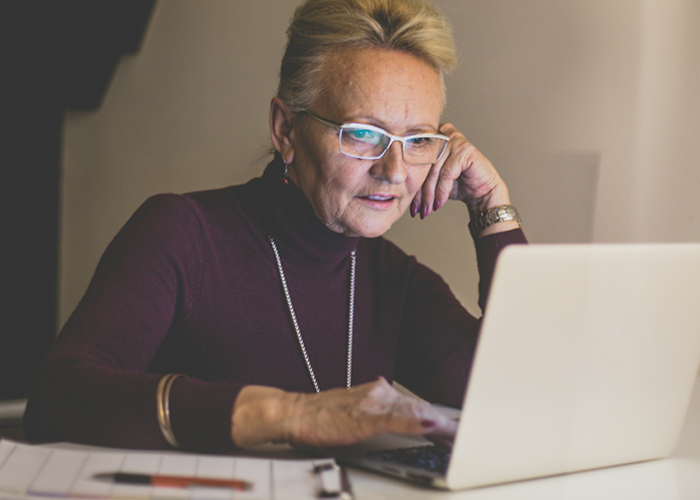 Older woman wearing glasses working on a laptop late at night, illustrating server down business hours malicious compliance. Older woman wearing glasses working on a laptop late at night, illustrating server down business hours malicious compliance.