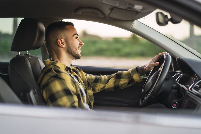 Young man driving a car, smiling and focused, illustrating doctors and nurses sharing haunting experiences today.