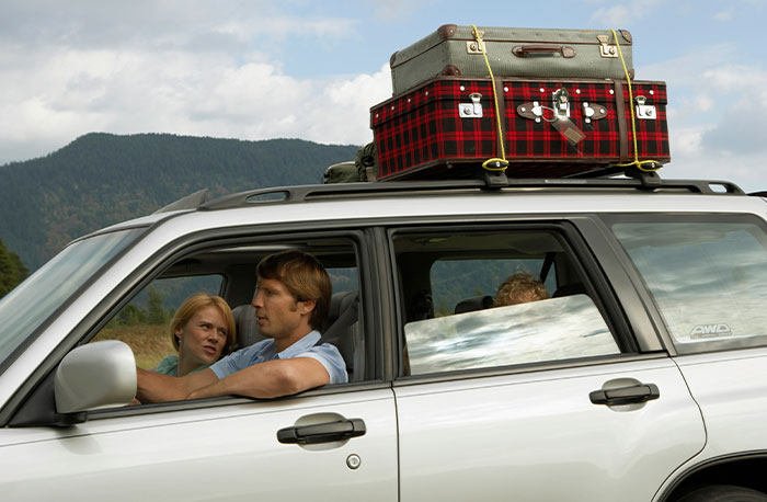 Family packing luggage on car roof, reflecting on school gossip and facts during a scenic trip in the mountains.