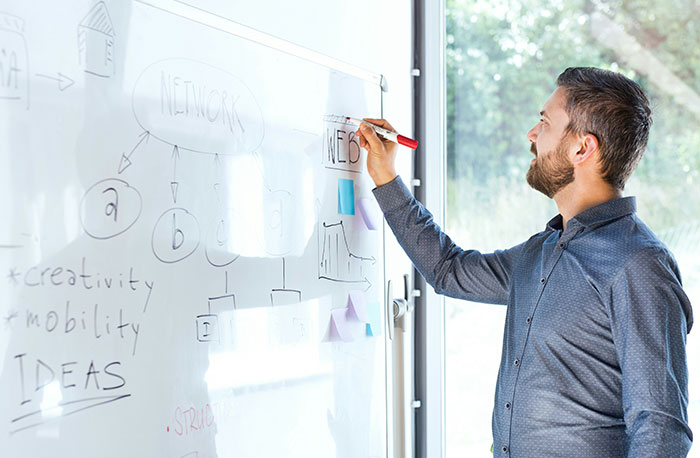 Man writing on whiteboard with network diagram, illustrating school gossip facts exposed in an open discussion setting