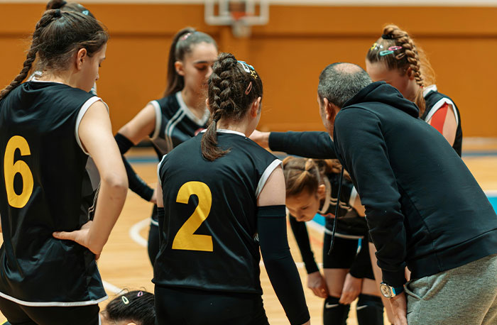 High school basketball team huddling with coach on court, illustrating school gossip and facts revealed in a team setting.