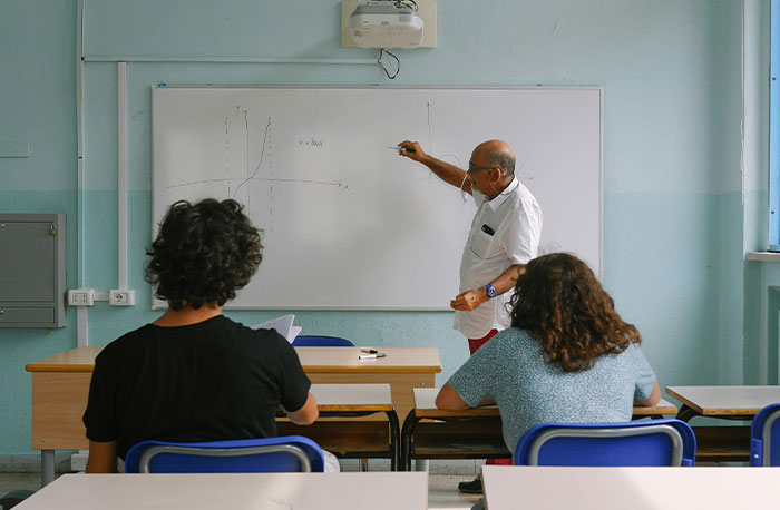 Teacher explaining a math graph on the whiteboard to students in a classroom, highlighting school gossip facts.
