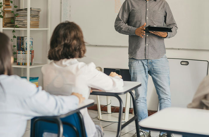 Teacher holding tablet while students listen in classroom setting illustrating school gossip turned out to be facts concept.