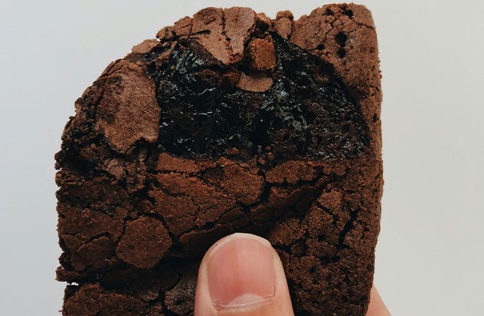 Hand holding a cracked chocolate brownie with a bite taken, illustrating school gossip turned out to be facts concept.