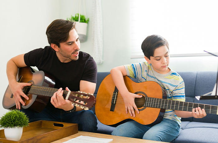 Man teaching boy to play guitar at home, capturing a moment of learning and school-related interaction.