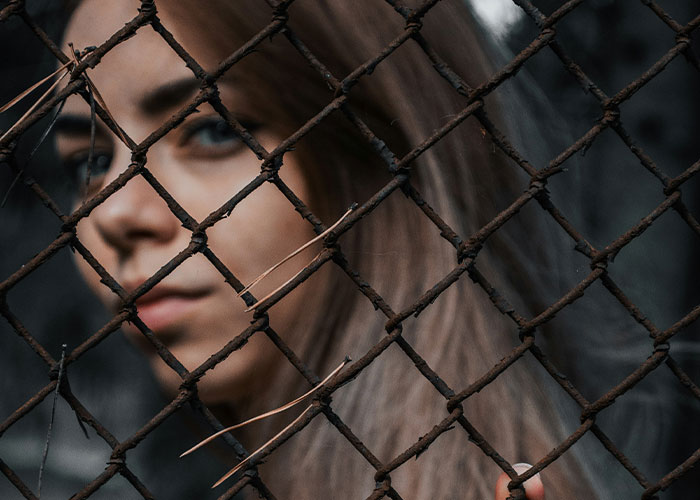 Young woman behind rusty fence, symbolizing dark secrets people found about their family members changing perceptions.