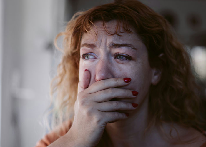 Woman with red hair covering her mouth, tearful and distressed, reflecting on dark secrets that changed family views.