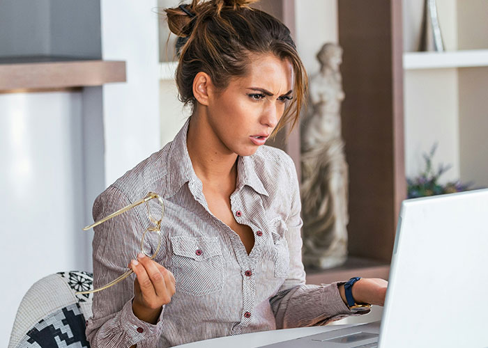 Young woman holding glasses, looking surprised and confused while discovering dark secrets about family members on laptop.
