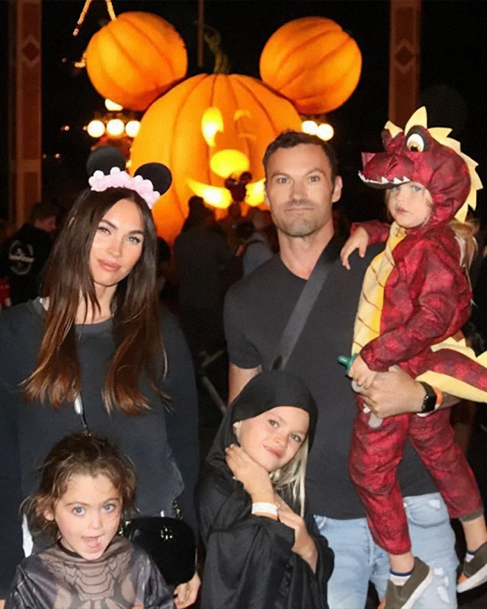 Family dressed in Halloween costumes at night with large pumpkin decoration, relating to Dancing With The Stars pro controversy.