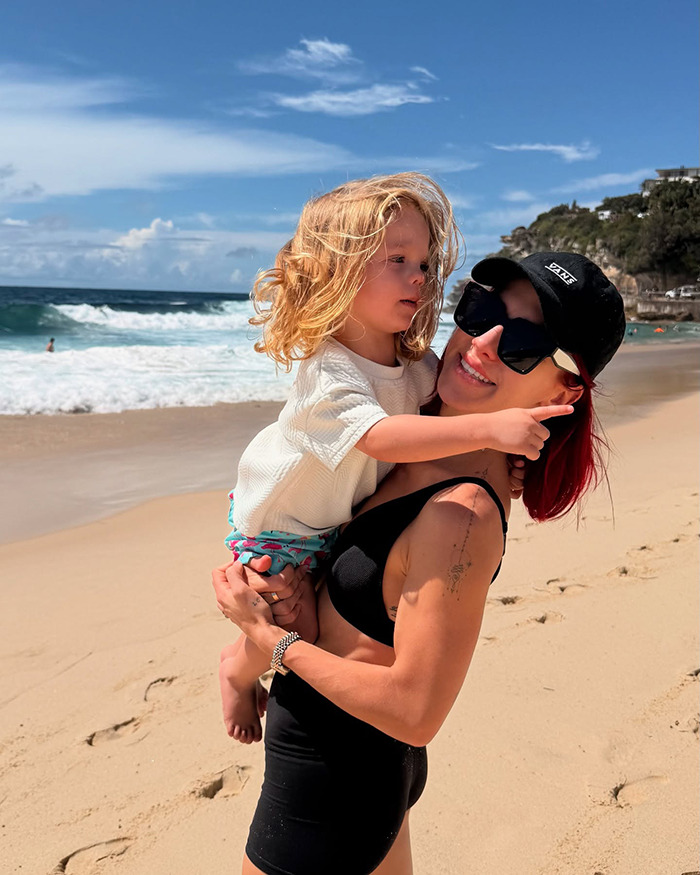 Dancing With The Stars pro holding her young son at the beach with waves and cliffs in the background.