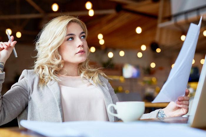 Young woman reviewing documents in a cafe, illustrating feelings about nephew's first birthday baby shower plan.