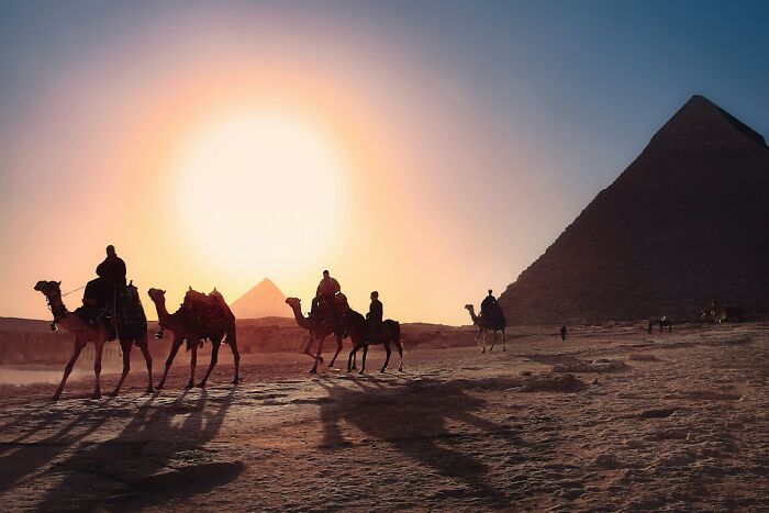 People riding camels near pyramids at sunset, showcasing travel destinations seen in person versus pictures.