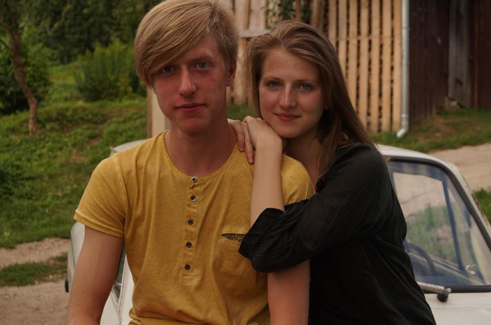 Young couple sitting together outdoors near a car, portraying sister boyfriend relationship drama with a thoughtful mood.