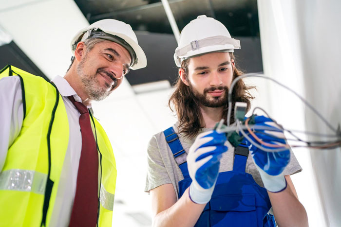 Two construction workers wearing helmets inspecting electrical wiring inside a building under renovation site. Two construction workers wearing helmets inspecting electrical wiring inside a building under renovation site.