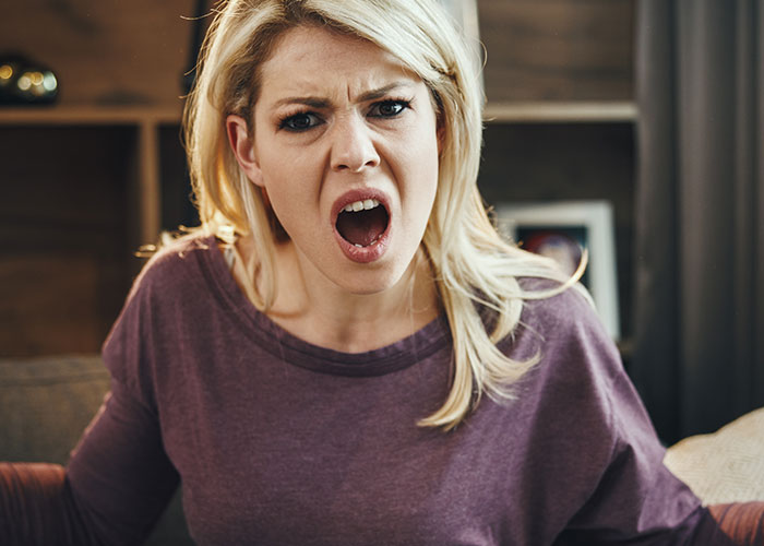 Woman angrily shouting indoors with upset expression, visualizing sister threatening to call the cops scenario.