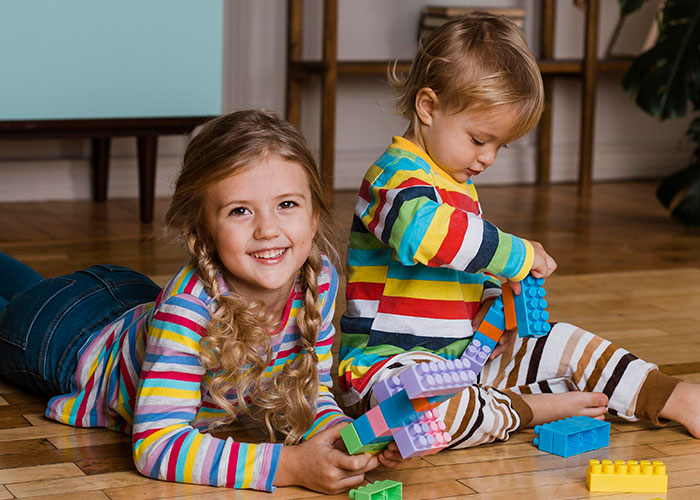 Two kids playing with colorful blocks on the floor, illustrating sister threatens to call the cops scenario.