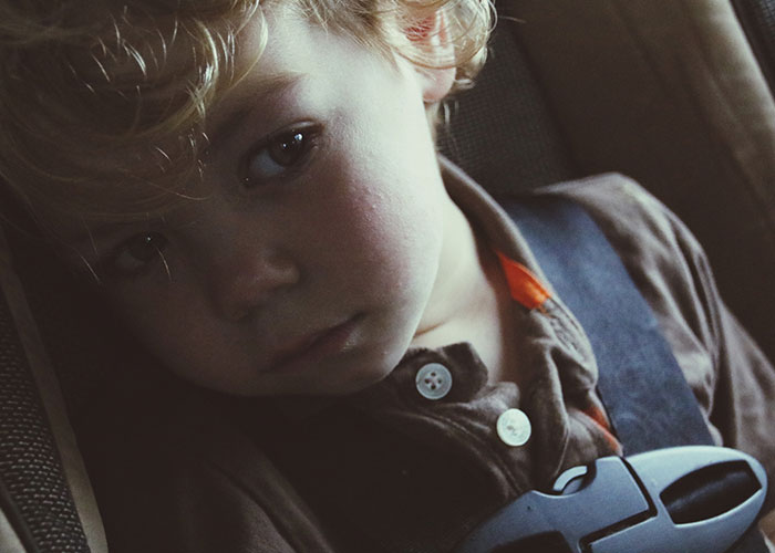 Young child looking sad and thoughtful sitting in a car seat, representing sister threatens to call the cops situation.