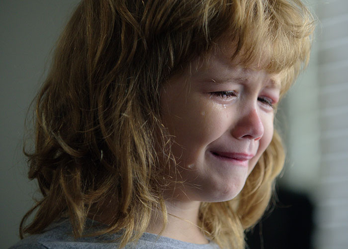 Young girl crying with tears on her face, showing emotional distress related to sister and kids home conflict.