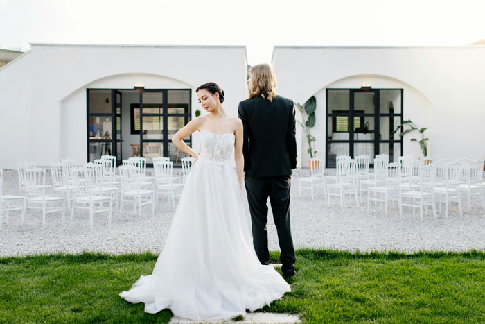 Bride in wedding dress standing back-to-back with groom outside, reflecting tension and family favoritism during ceremony.