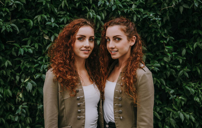 Two red-haired twin sisters standing close together outdoors, illustrating bride tries to erase twin at wedding.
