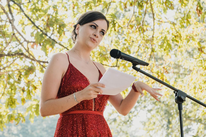 Bride in a red dress giving a speech at an outdoor wedding, highlighting family favoritism and twin rivalry.