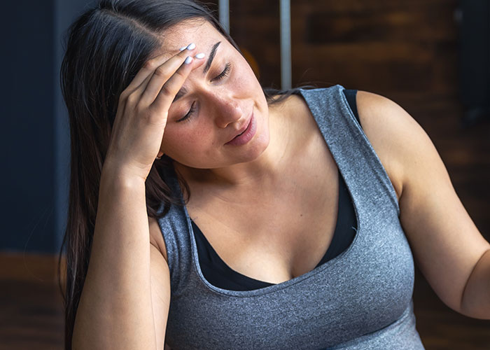 Woman in a gray tank top looking thoughtful and stressed, reflecting on her body and personal transformation journey.