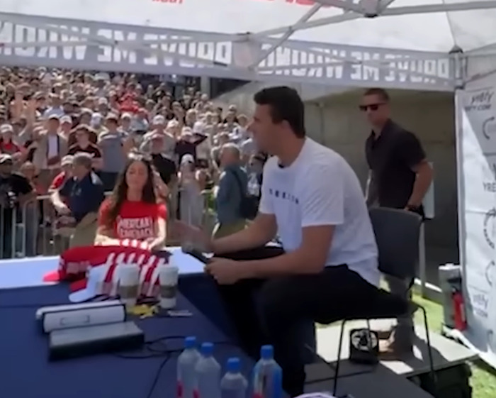 Man sitting at a table signing items for a crowd at an outdoor event with South Park viewers reacting to Charlie Kirk episode.