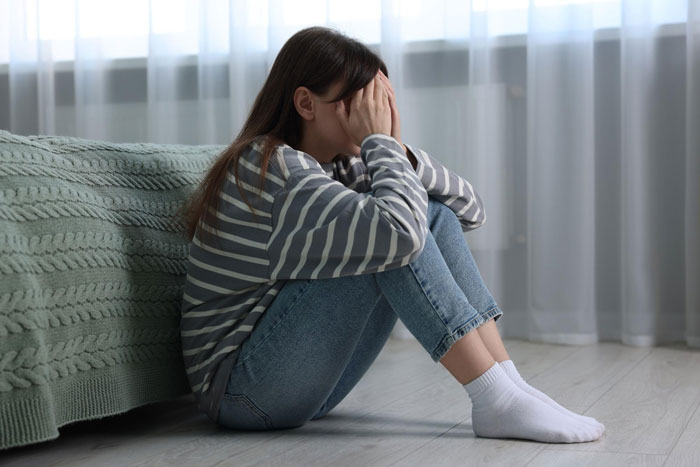 Young woman sitting on the floor with head in hands, distressed and worried about parents' food making her sick.