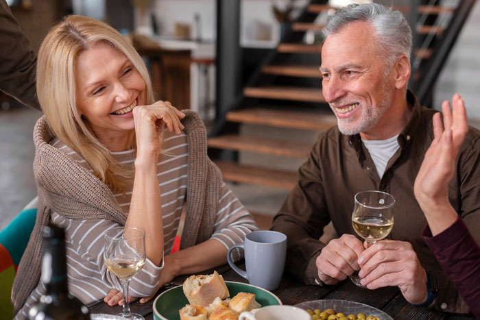 Middle-aged parents enjoying food and drinks at a table while their daughter worries about getting sick from their meals.