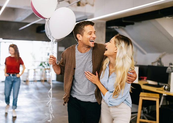 Happy couple laughing and holding balloons indoors as partner secretly observes, illustrating crazy ways people found out cheating.